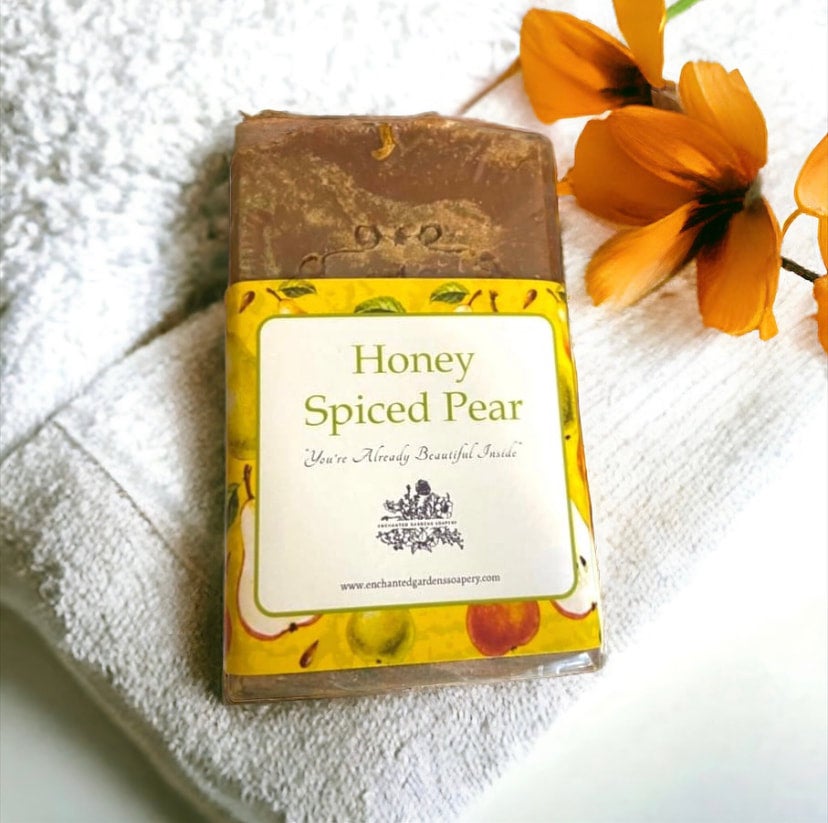A bar of Honey Spiced Pear soap with a yellow label, placed on a white towel with a orange flower in the background.