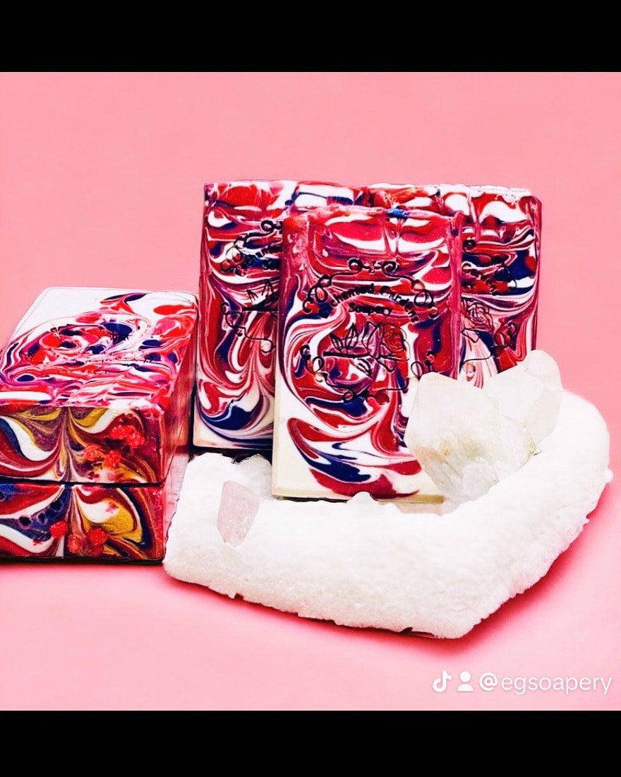 Three bars of handmade rose quartz soap with a floral pattern in a pink background, alongside a white silk cloth.