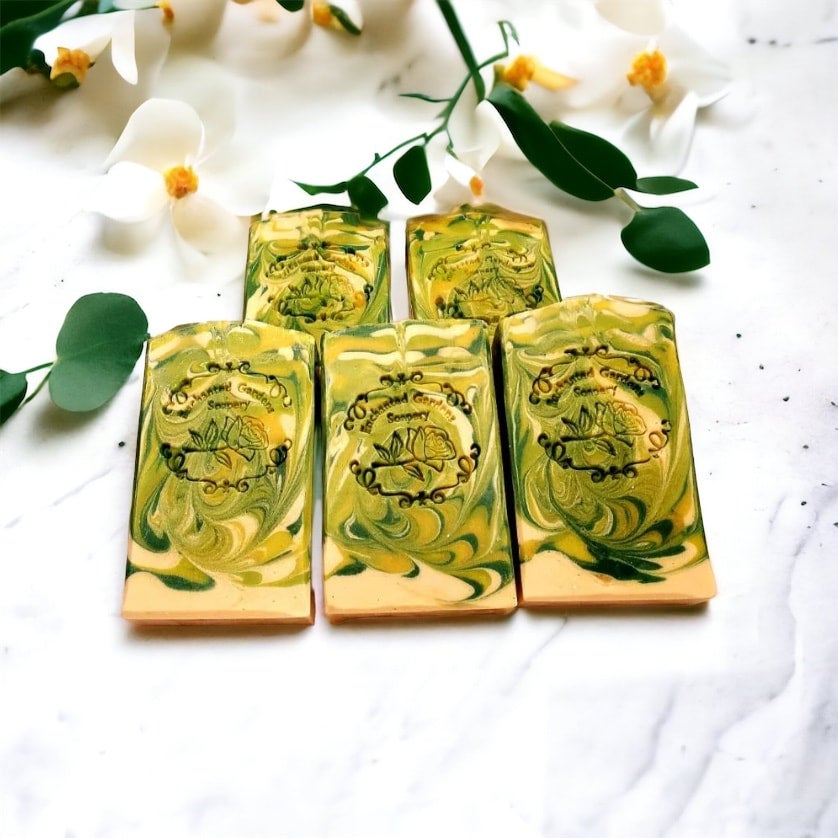 A set of bar soaps with a green and yellow marbled design, displayed on a white surface, surrounded by leaves and flowers.