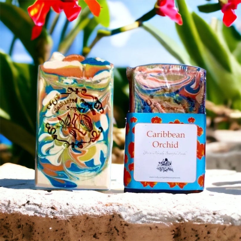 A colorful bar of handmade soap with a floral pattern, labeled 'Caribbean Orchid', placed on a stone surface with a vibrant plant in the background.